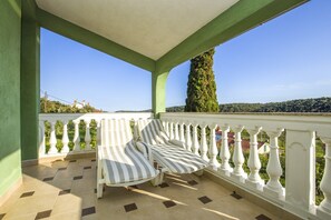 Een overdekt balkon met gestreepte ligstoelen, een betegelde vloer en een witte balustrade.