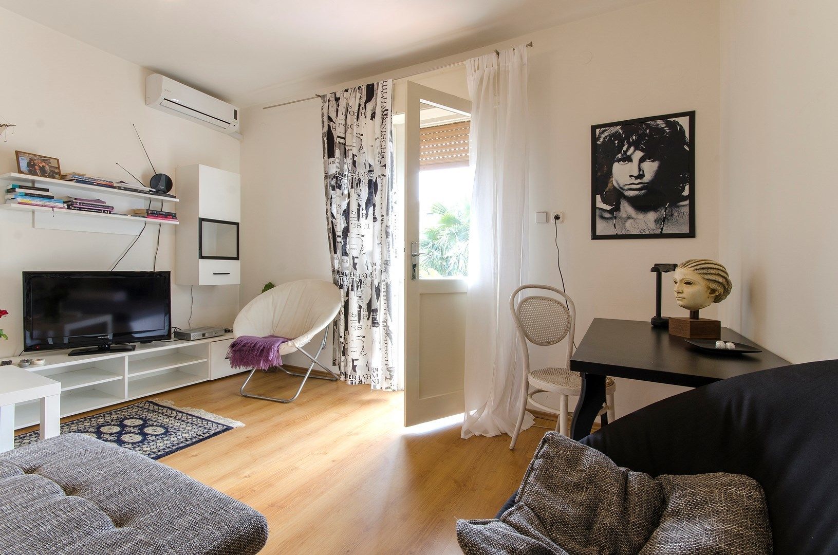 En moderne stue med et fladskærms-tv, en hvid stol, en sort sofa og et spisebord med en buste.