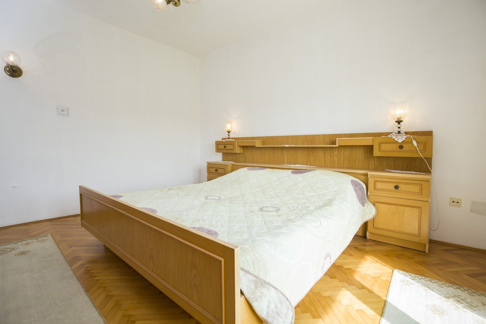 A bedroom with a wooden bed, bedside tables, and wall-mounted lamps.