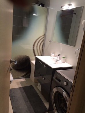 Un baño pequeño con cabina de ducha de vidrio, lavadora y lavabo con espejo.