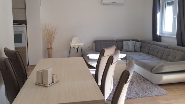 Un salon moderne avec un coin repas, un canapé gris, une table blanche et une cuisine en arrière-plan.