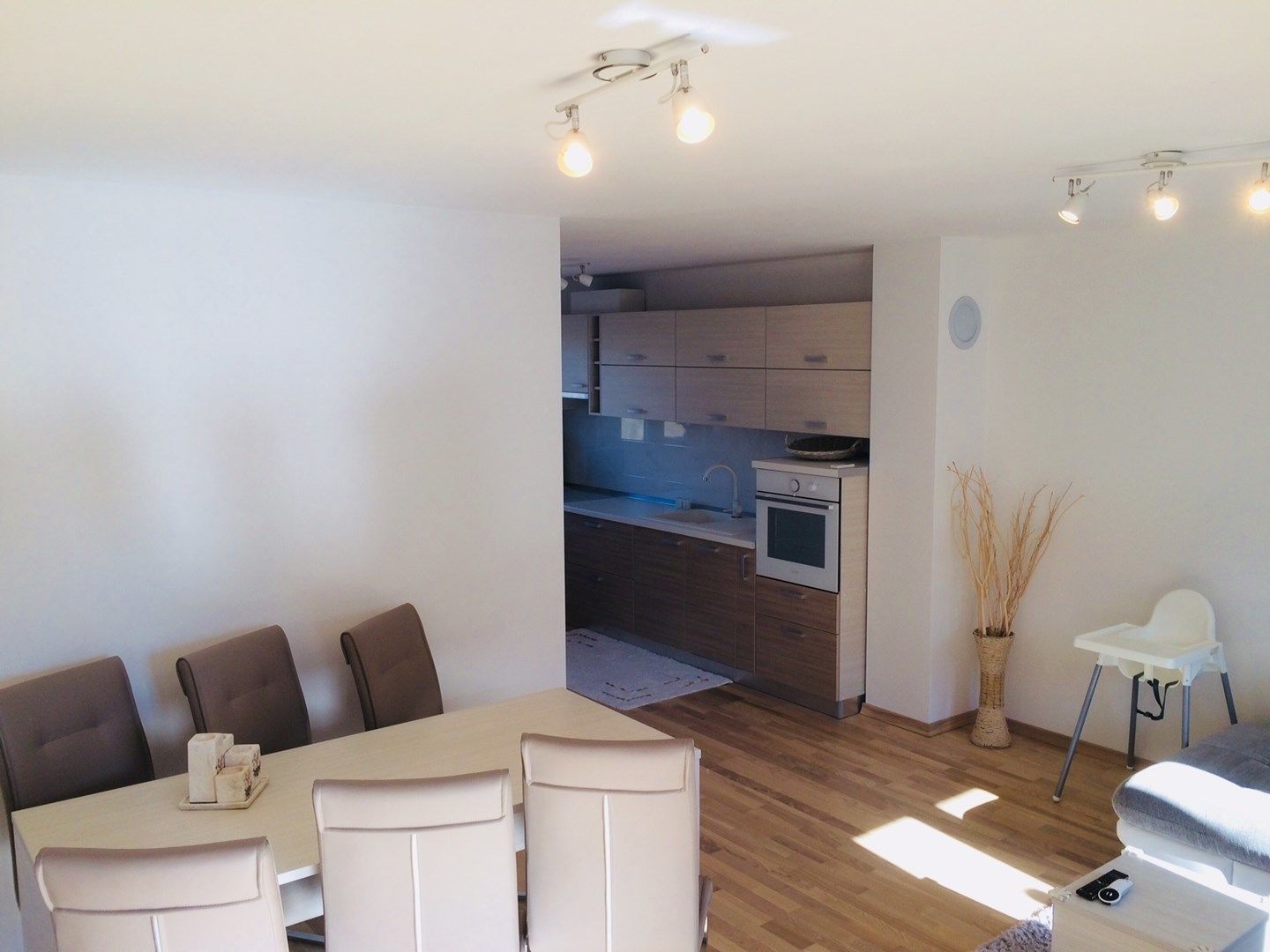 Una habitación moderna y bien iluminada con comedor, kitchenette y una sala de estar con una pequeña mesa y sillas.