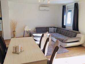 Una sala de estar moderna con sofá, mesa de comedor, sillas y una pequeña mesa blanca con un florero.