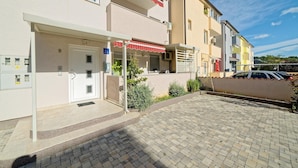 Un immeuble résidentiel doté d’une cour pavée, d’une porte avec une enseigne et d’un petit espace extérieur aménagé pour s’asseoir.