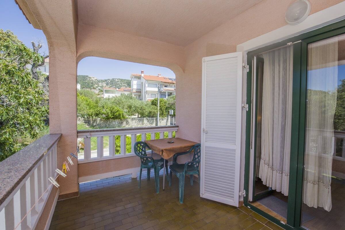 Varanda com mesa e cadeiras, porta de correr de vidro e vista para edifícios e áreas verdes.