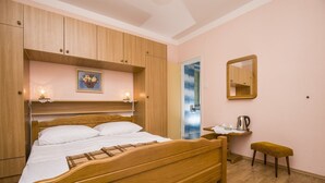 A bedroom with a wooden bed, a bedside table with a kettle, a small stool, and a mirror on the wall. - Rooms Anđela Banjol (Rab)