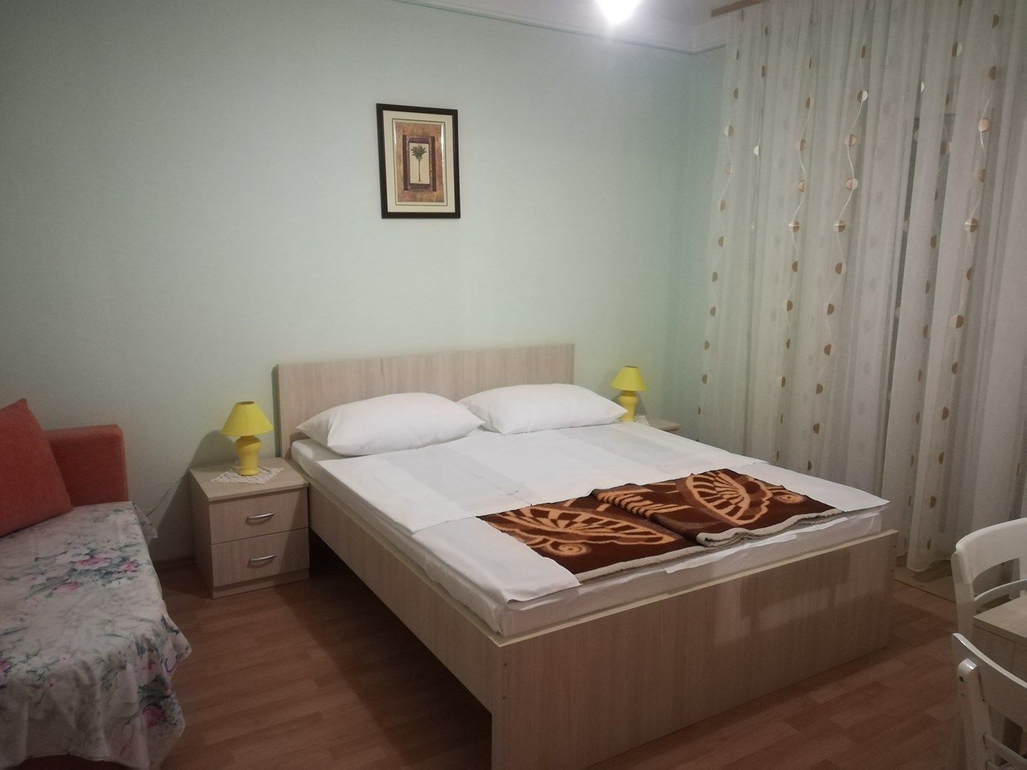 A single-bed room with a wooden headboard, two bedside lamps, a small bedside table with drawers, a floral-patterned bedspread, and a decorative throw blanket.