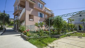 A two-story residential building with a balcony and a garden area with flowers and plants. - Rooms Anđela Banjol (Rab)