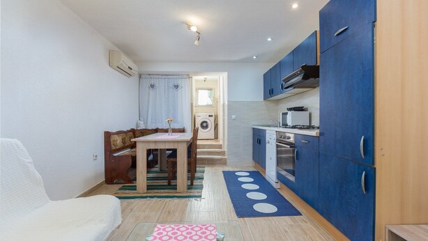 A compact kitchen with blue cabinets, a dining area with a table and chairs, and a small kitchenette. - Apartment Arena (Pula)
