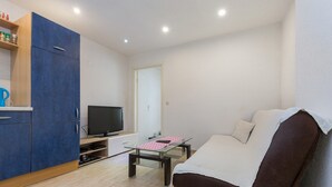 A compact living space with a sofa, a television, a small table, and a cabinet with kitchen items. - Apartment Arena (Pula)
