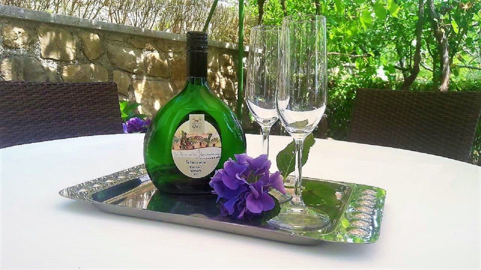 Eine Weinflasche und zwei Gläser auf einem Tablett mit violetten Blumen.