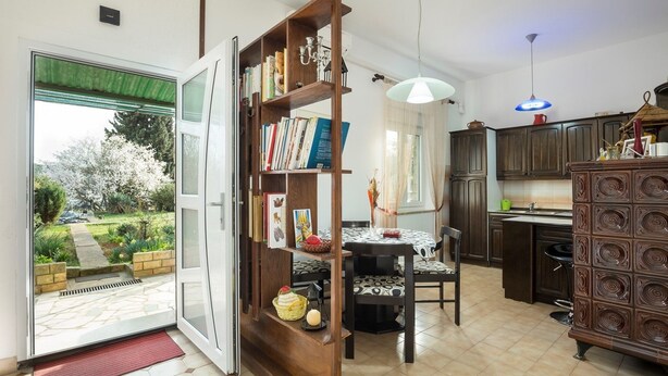 A spacious kitchen with dark wooden cabinets, a dining area with a table and chairs, and a large bookshelf filled with books. - Apartment Lili Pula (Pula)