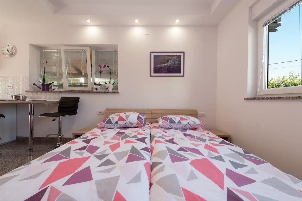 Un dormitorio con dos camas, un escritorio, una silla, un ventanal con persianas, un reloj y un cuadro en la pared.