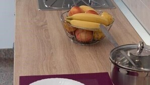 Eine Küchenarbeitsplatte mit Obstkorb, Spüle und Topf auf einer violetten Matte.
