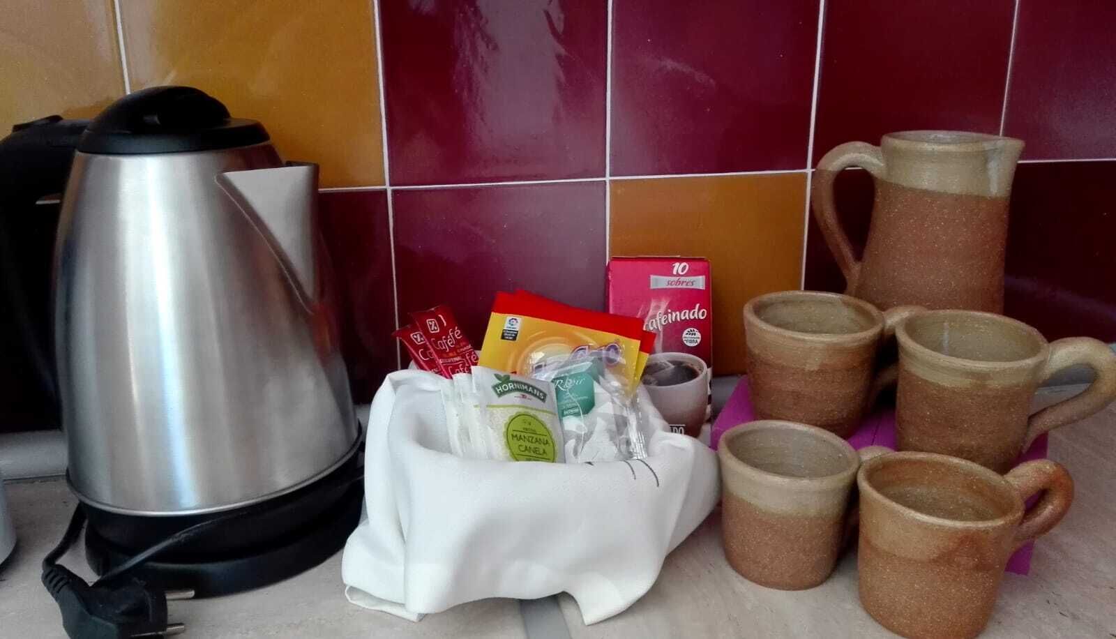 A kitchen counter with a stainless steel kettle, a white cloth with food items, and several brown ceramic mugs.