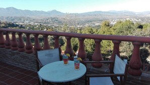 Ein Balkon mit Tisch und Stühlen, mit Blick auf eine gebirgige Landschaft.