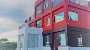 A modern multi-story house with a red and white facade, large windows, and a visible outdoor seating area. - The Song of Eagle (Donghe)