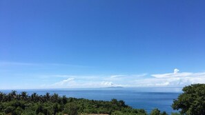 A coastal landscape with a clear sky, dense greenery, and a view of the sea.