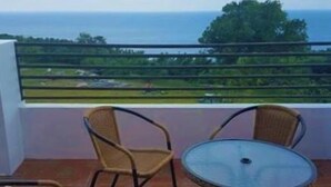 A balcony with wicker chairs and a glass table, overlooking a coastal landscape. - The Song of Eagle (Donghe)