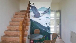 A staircase with a mural of an eagle in flight, a small round table, and a chair. - The Song of Eagle (Donghe)