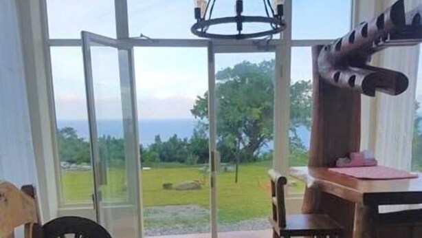 A room with a large glass door leading to a scenic outdoor view, a wooden dining table with chairs, and a hanging light fixture. - The Song of Eagle (Donghe)
