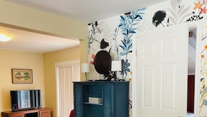 A living room with a glass coffee table, red armchair, blue cabinet, and a door with floral wallpaper.