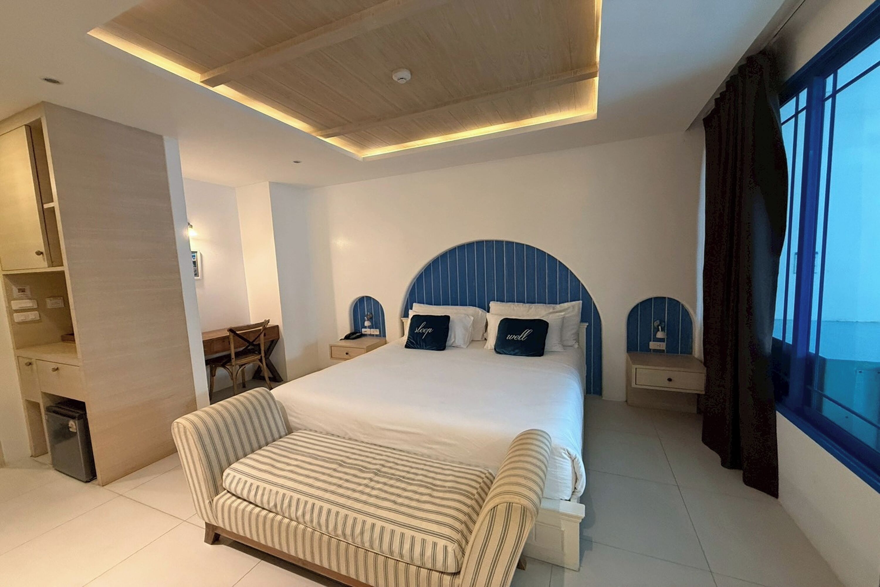 A modern hotel room with a large bed, a sofa, a desk, and a view of the outside.