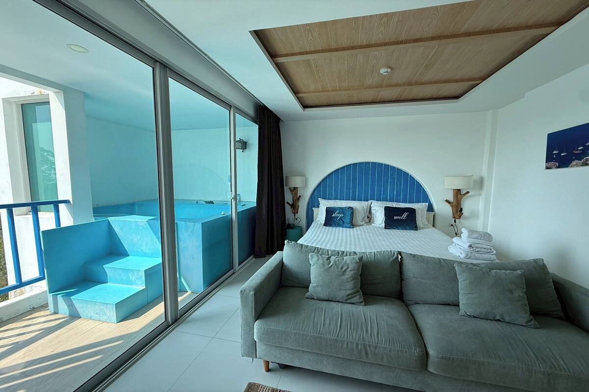Une chambre avec un lit, un canapé, une grande fenêtre et un balcon.