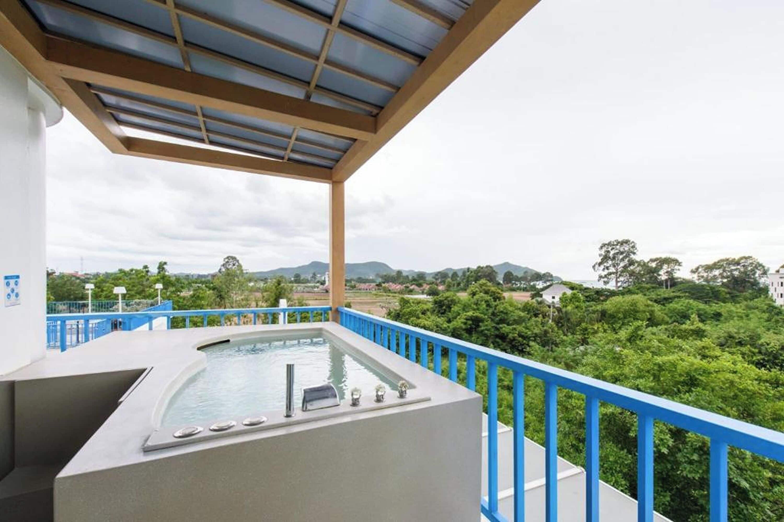 A balcony with a hot tub, blue railing, and a view of greenery and hills.