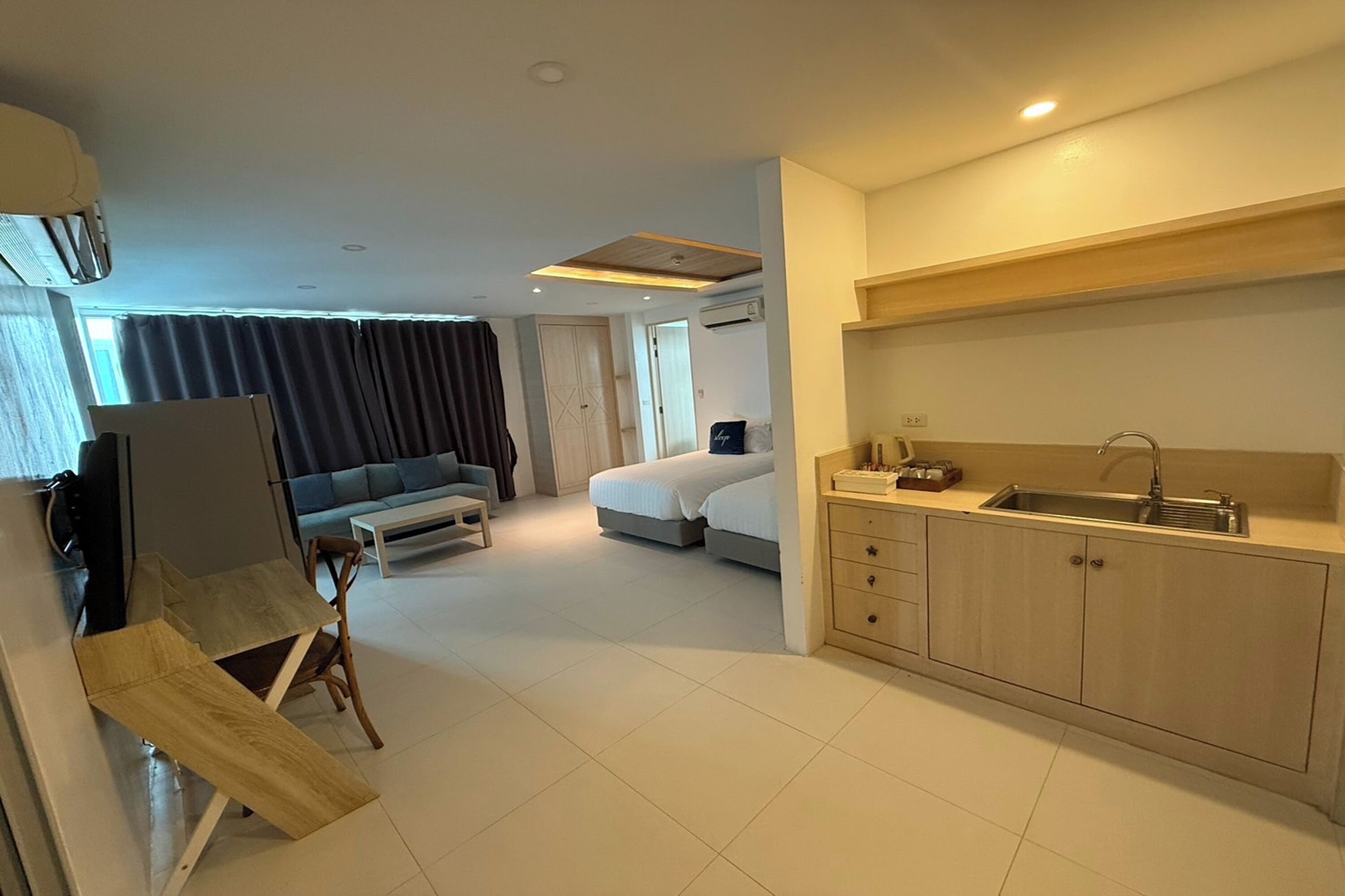 A compact hotel room with a kitchenette, a bed, a sofa, and a dining table.