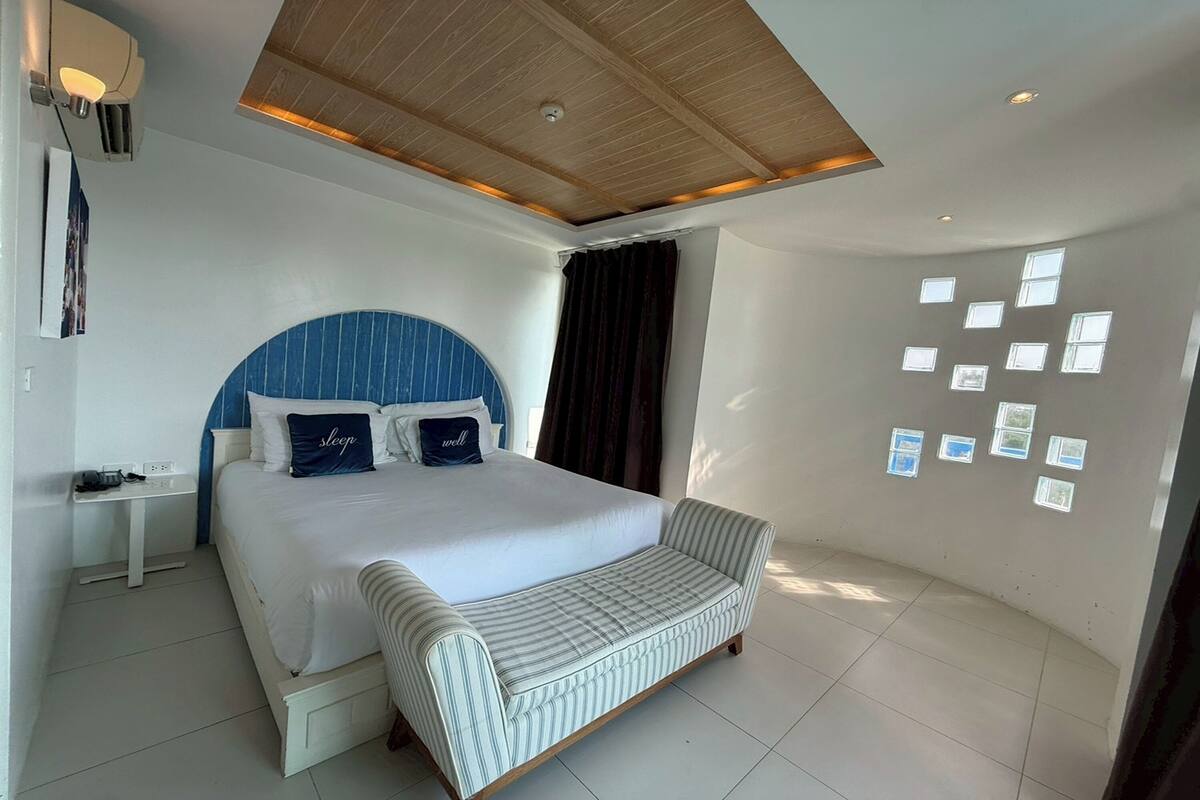 Une chambre moderne avec un grand lit, des tables de chevet, un banc et des tableaux accrochés au mur.