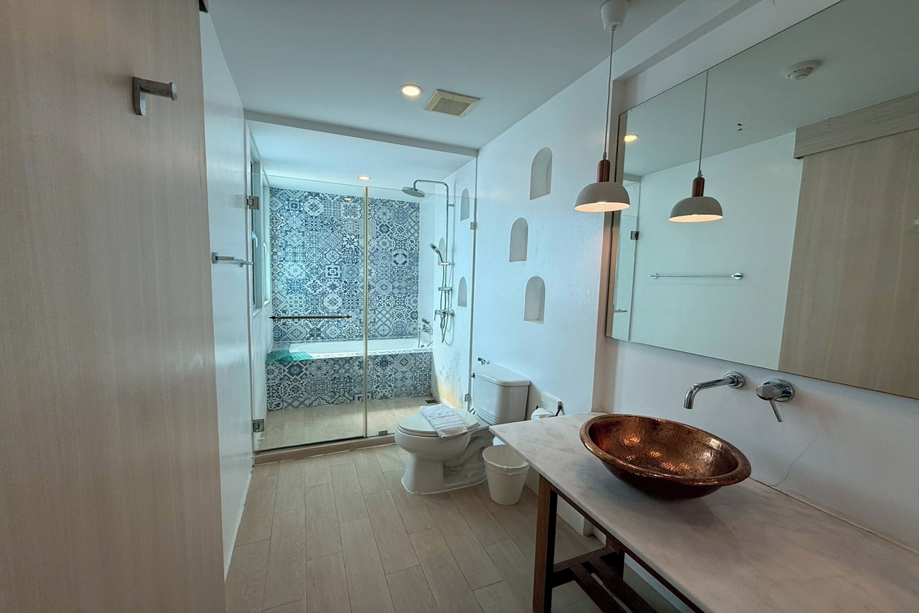 A modern bathroom with a glass shower enclosure, a white toilet, a copper sink, and a large mirror.