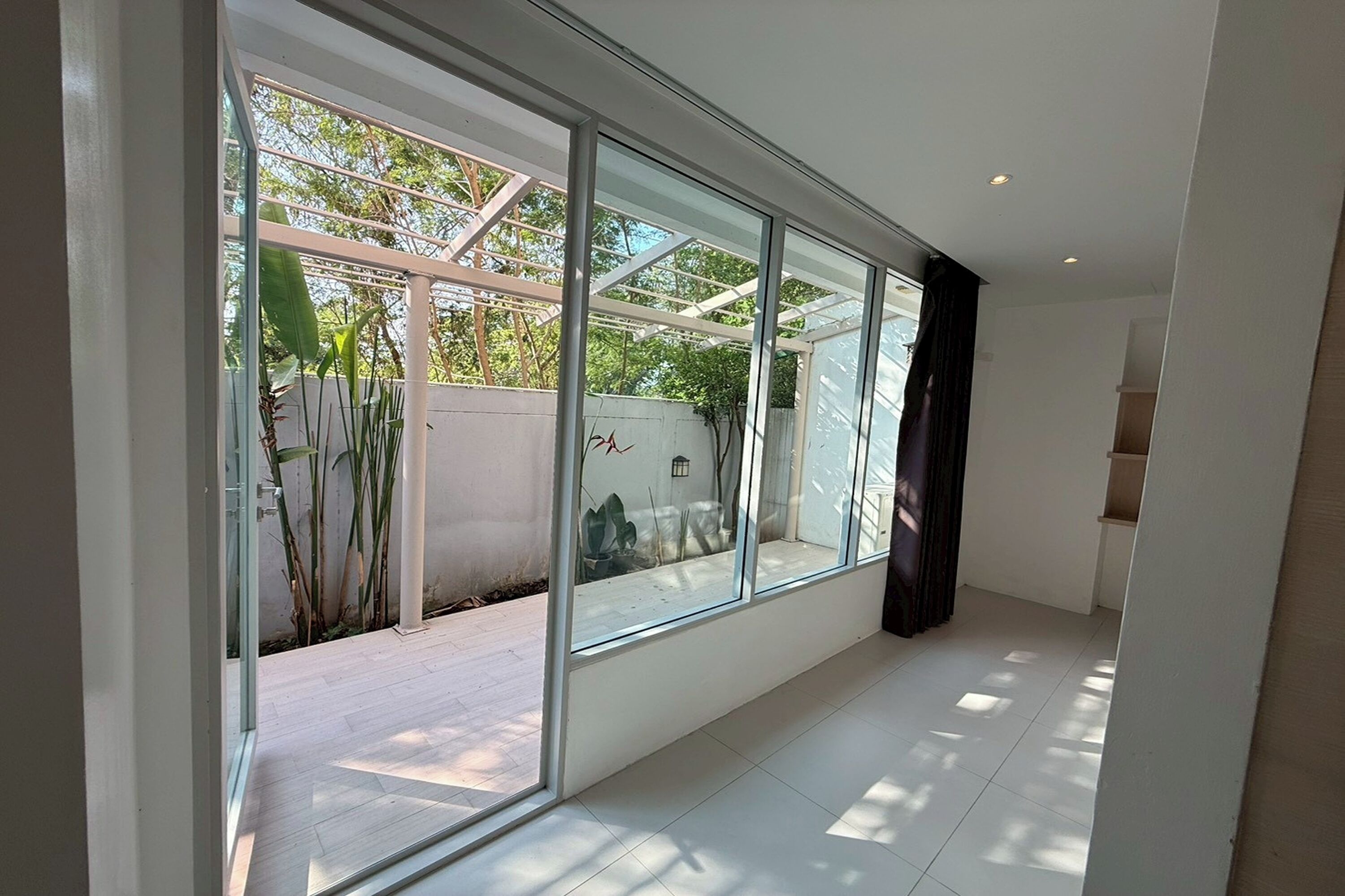 Una habitación con grandes ventanales, piso de baldosas y pared blanca.