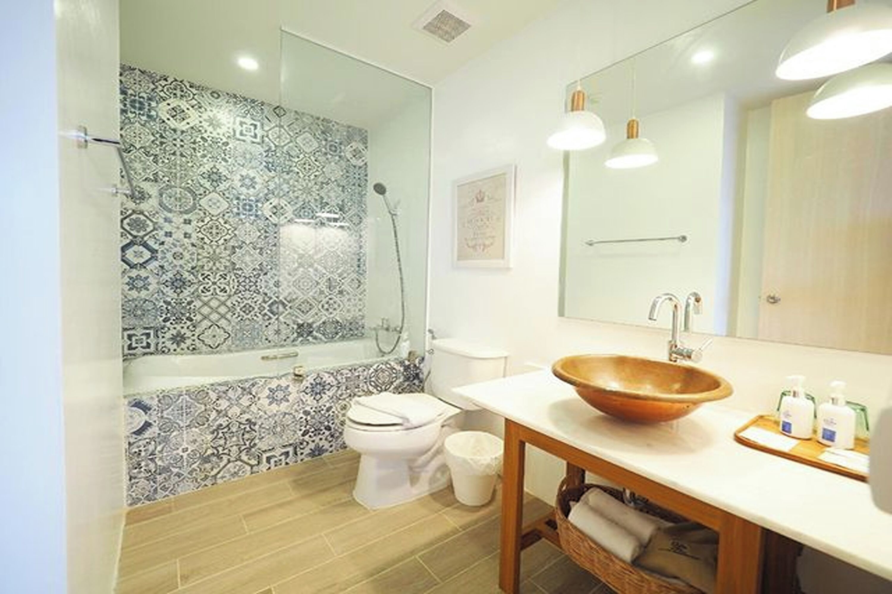 A bathroom with a patterned tile wall, a white toilet, a wooden sink, and a mirror.