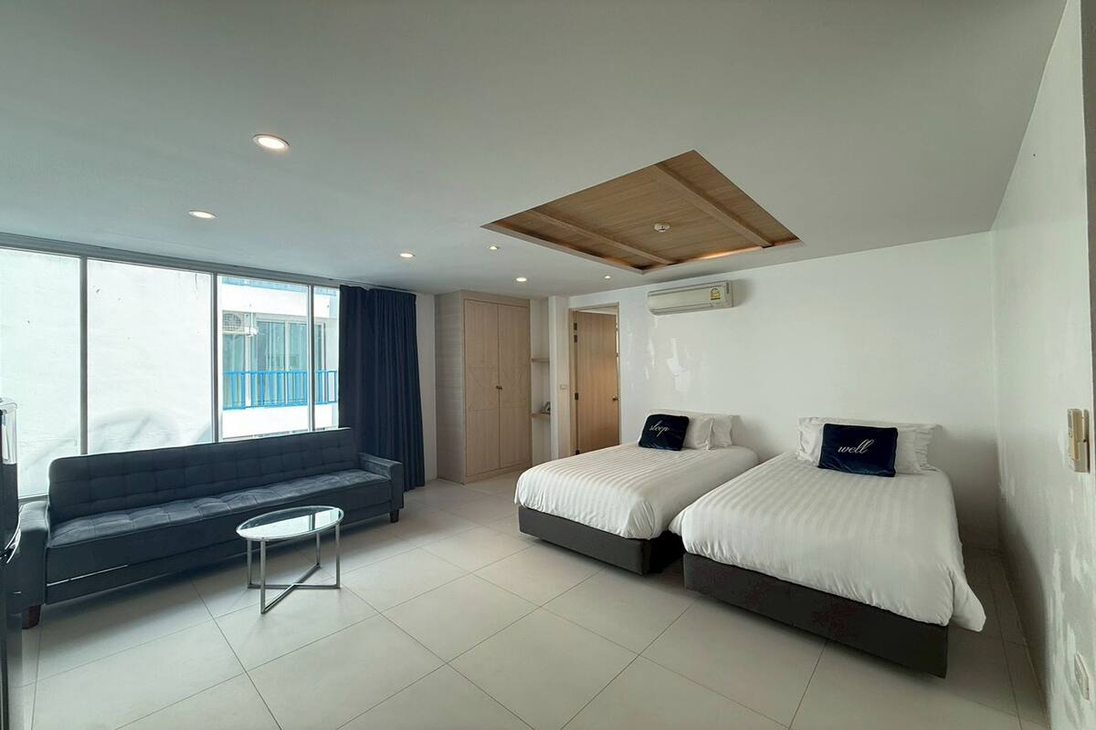 Une chambre d’hôtel moderne avec un canapé, deux lits, une petite table et une grande fenêtre.