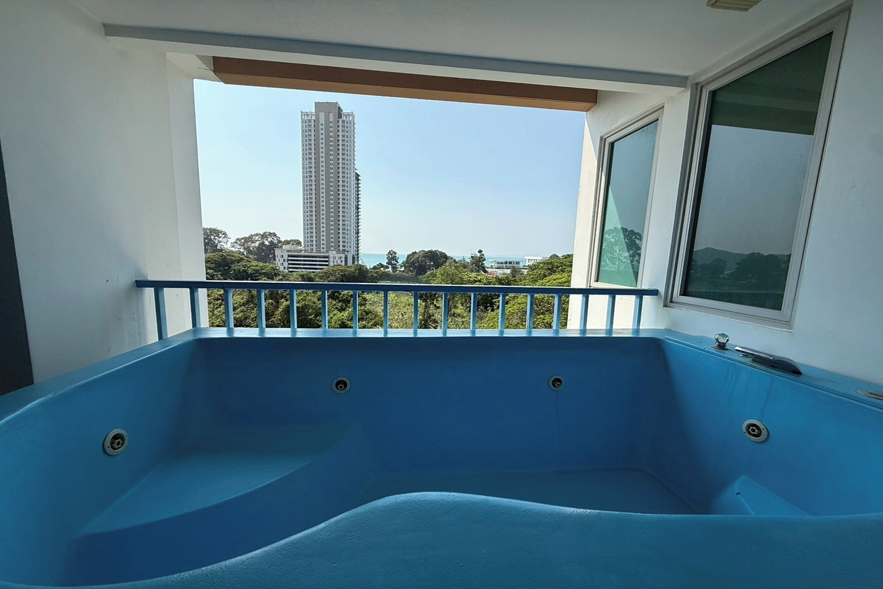 Ein blauer Whirlpool auf einem Balkon mit Blick auf ein hohes Gebäude und viel Grün.