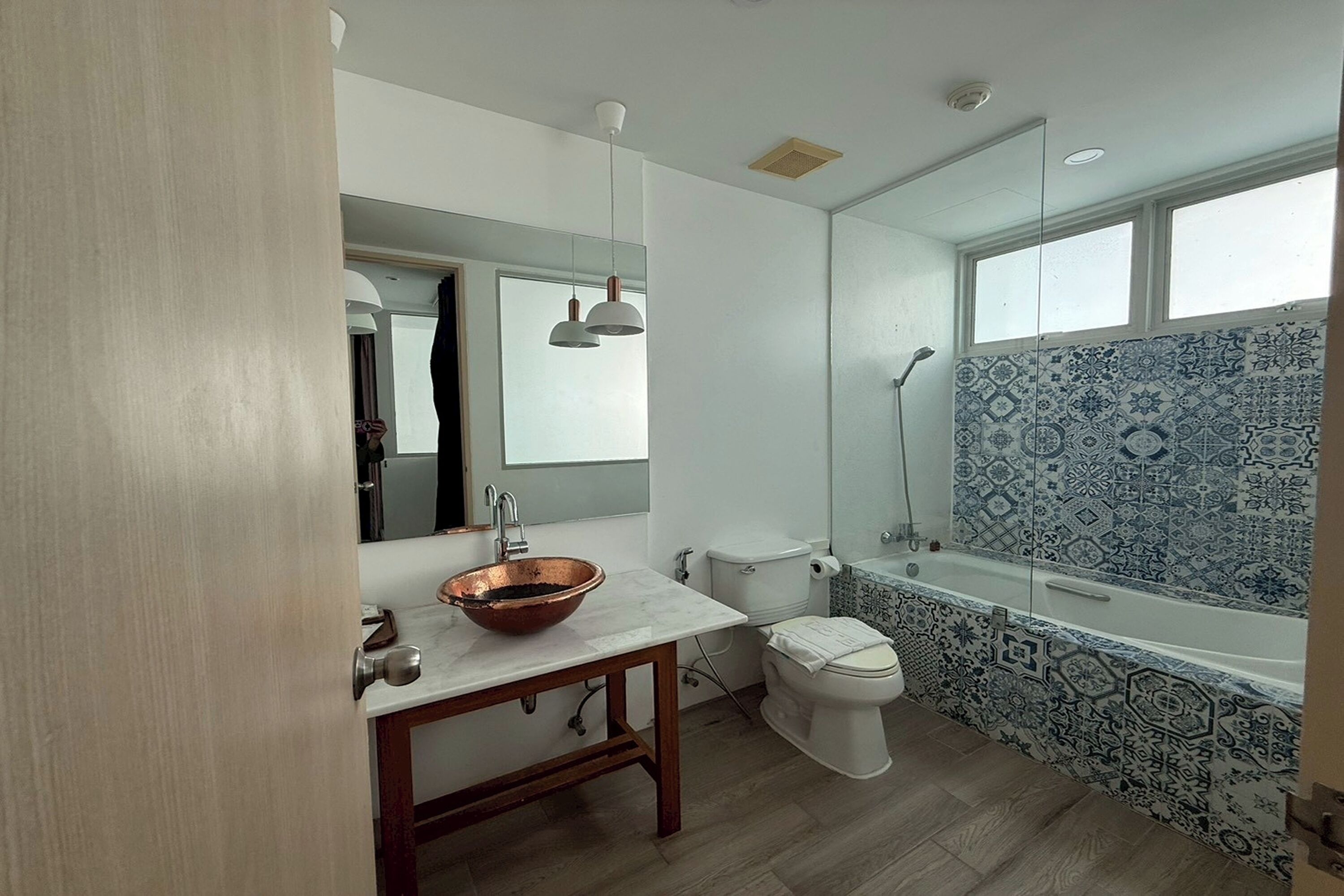 Une salle de bain avec un lavabo en cuivre, des toilettes blanches et une baignoire ornée de carreaux à motifs.