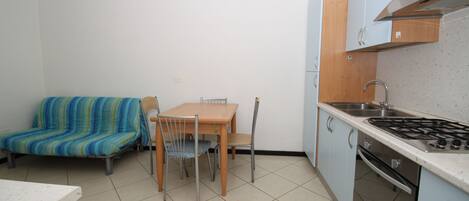 A compact kitchen with a dining table and chairs, a sofa, and a stove.