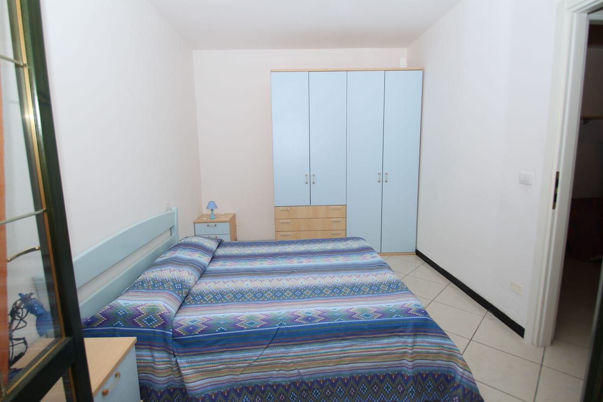 Un dormitorio pequeño con cama, mesita de noche, armario y puerta que da a otra habitación.