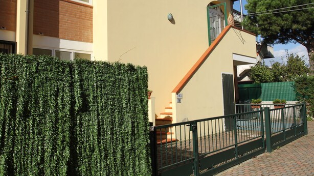Ein Wohngebäude mit heller Fassade, einem grünen Tor und einer Treppe, die zu einem Balkon führt.