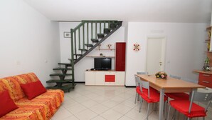 Ein Wohnzimmer mit einer Couch, einem Fernseher, einem Esstisch, Stühlen und einer Treppe.