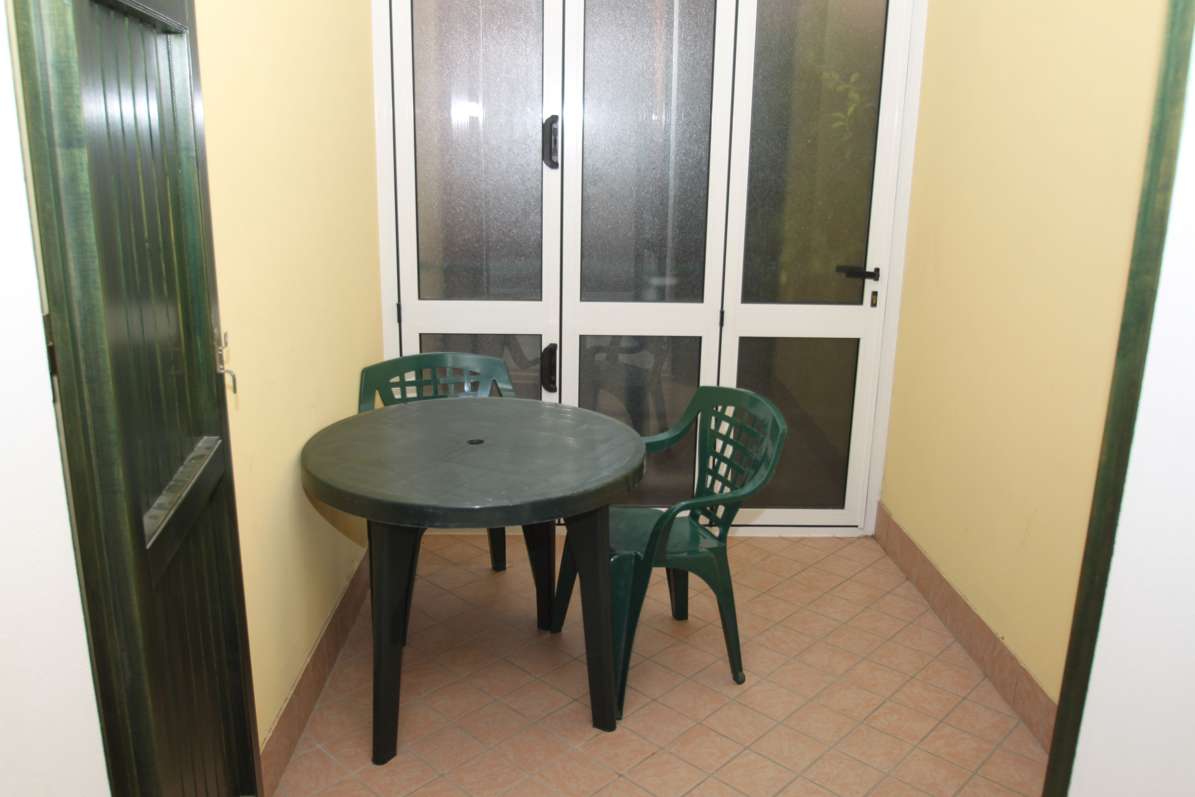 A small dining area with a round table and two chairs, a sliding glass door, and a tiled floor.