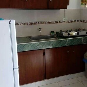 A kitchen with a refrigerator, stove, sink, and wooden cabinets. - Posada Rocky 2 (San Andrés)