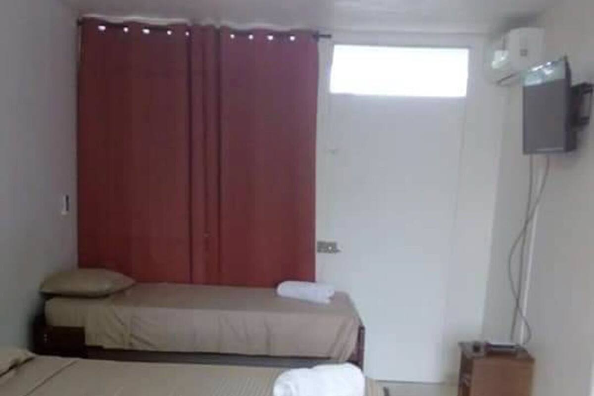 Une chambre avec deux lits, un téléviseur fixé au mur et une fenêtre avec des rideaux.
