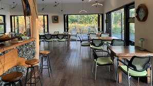 A spacious dining area with wooden tables and chairs, a large tree trunk centerpiece, and large windows offering a view of greenery. - Coconut Beach Homestay (Beinan)