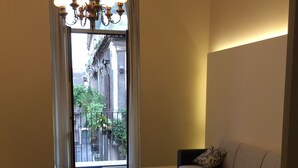 A hotel room with a bed, a sofa, a patterned floor, a chandelier, and a view of buildings through a window. - home in the historic center of Catania (Catania)