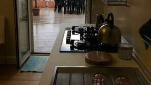 A compact kitchen with a gas stove, kettle, and a small sink. A sliding glass door leads to an outdoor patio with a table and chairs. - home in the historic center of Catania (Catania)