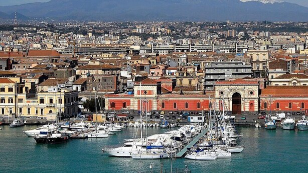 A coastal city with a marina filled with boats, historic buildings, and a prominent snow-capped mountain in the background. - home in the historic center of Catania (Catania)