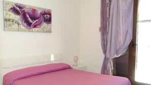 A bedroom with a bed, a nightstand, a lamp, a painting, and a window with curtains. - B&B Soleluna (Veglie)