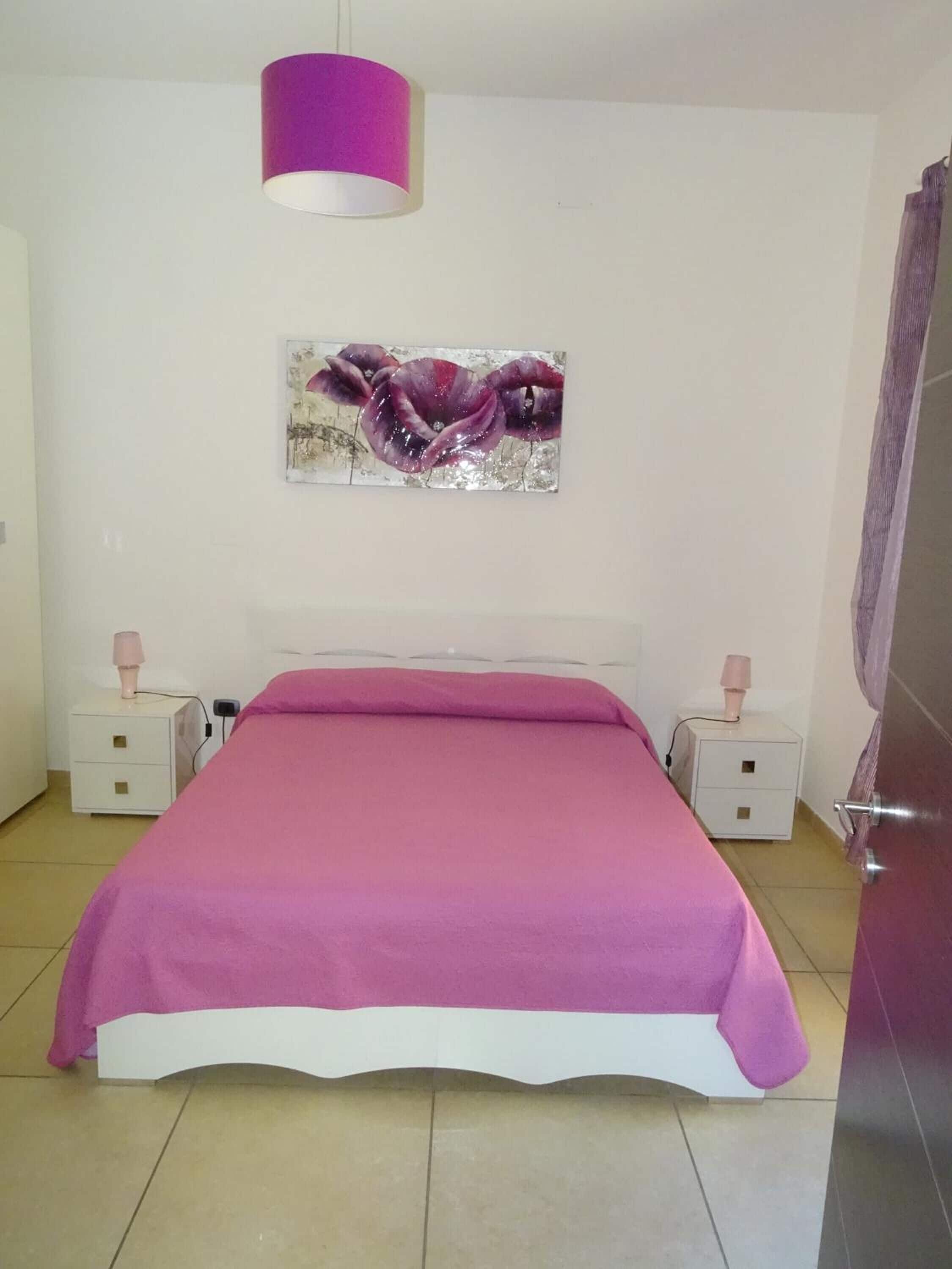 Een slaapkamer met een bed, twee nachtkastjes, een wandlamp en een schilderij.